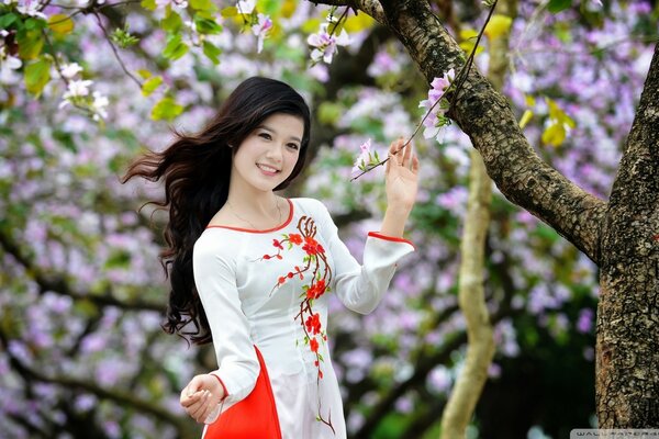 Dziewczyna w czerwono-białej sukience w pobliżu pięknych drzew