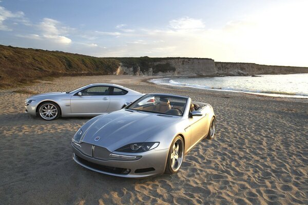 Two silver cars on a sandy beach