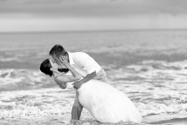 Blanco y negro novio besa a la novia en la orilla del mar