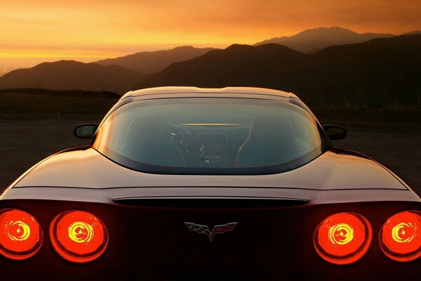 Auto hinten mit eingeschalteten Scheinwerfern im Hintergrund des Sonnenuntergangs