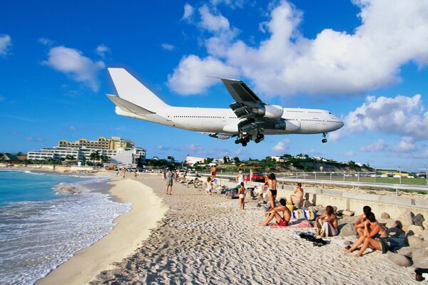 The plane flies over the beach with people