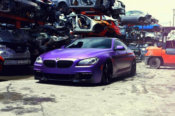 A purple understated BMW on black alloy wheels stands at the car recycling site