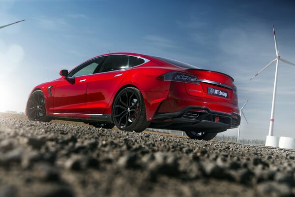 Red Tesla car standing against the background of windmills