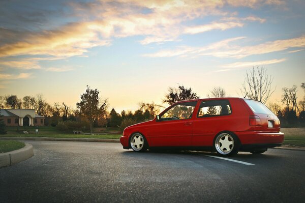 A red Volkswagen is driving on a winding road