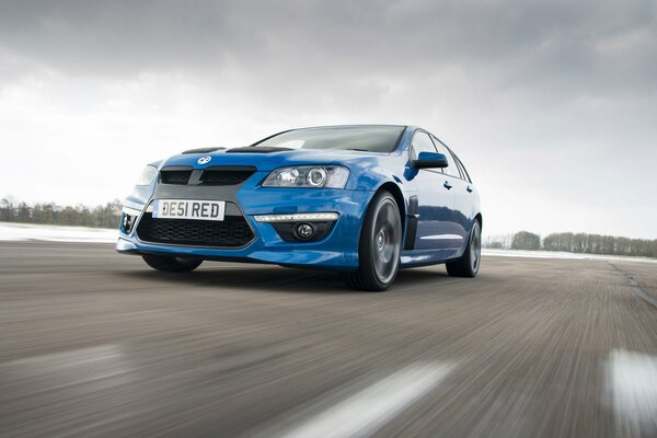 A blue car is driving at high speed on a winter road