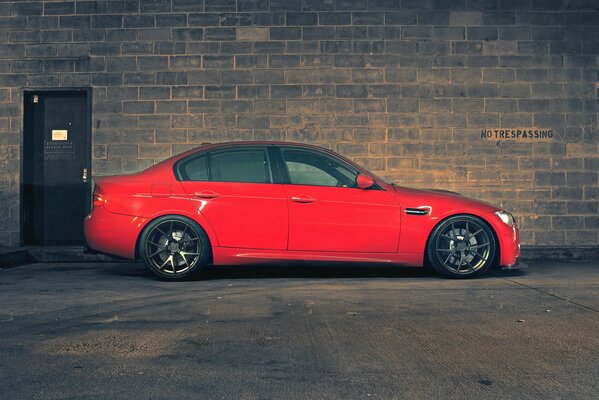 A red BMW stands in profile against a brick wall