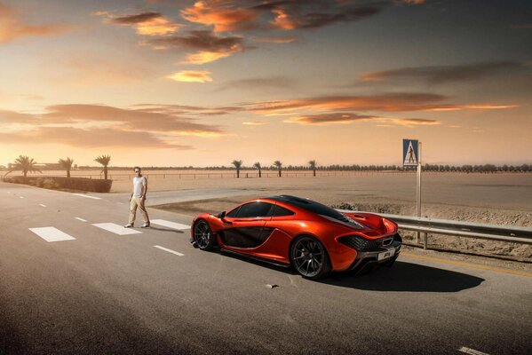 Supercar rossa sulla strada tra il deserto di fronte a un passaggio pedonale seguito da un uomo