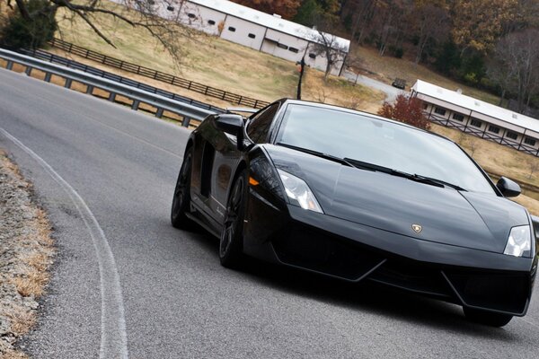 Ein schwarzer Lamborghini fährt auf der Straße mit Stoßstangen an den Rändern vor dem Hintergrund einer rustikalen Herbstlandschaft