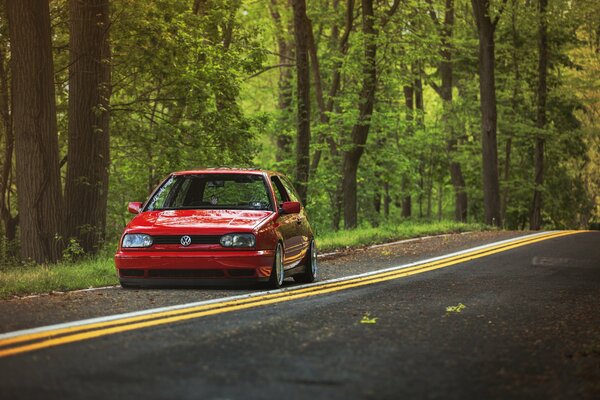 A red Volkswagen is driving on a road in the woods