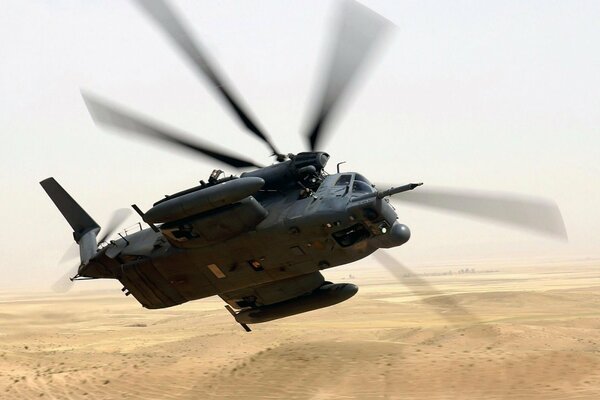 A heavy black military helicopter takes off from the desert