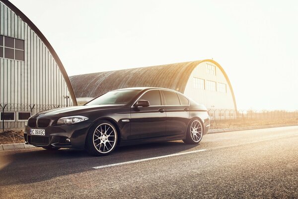 A black BMW car is standing on the highway under the sun