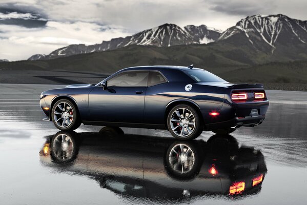 A black passenger car stands against the background of mountains, reflected in the surface of the water