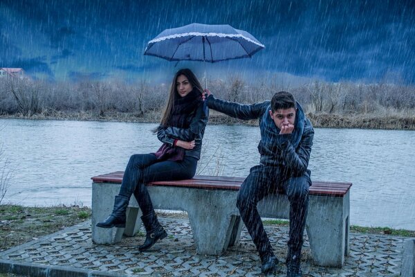 Chica y chico se sientan en un banco bajo la lluvia