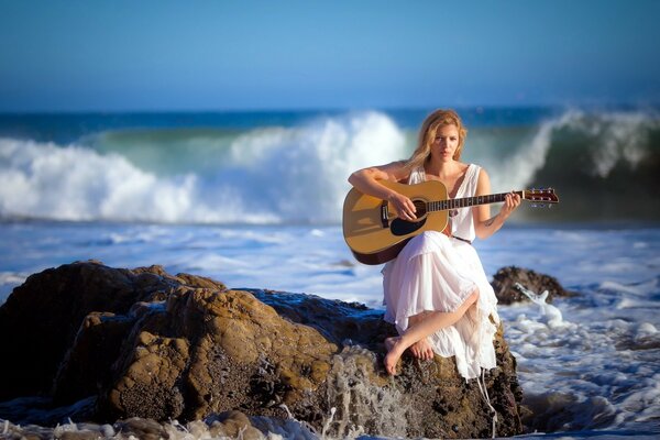 Chica con guitarra en una piedra en la orilla del mar