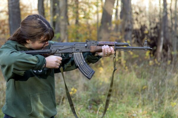 A girl with an ak-47 machine gun shooting in the woods
