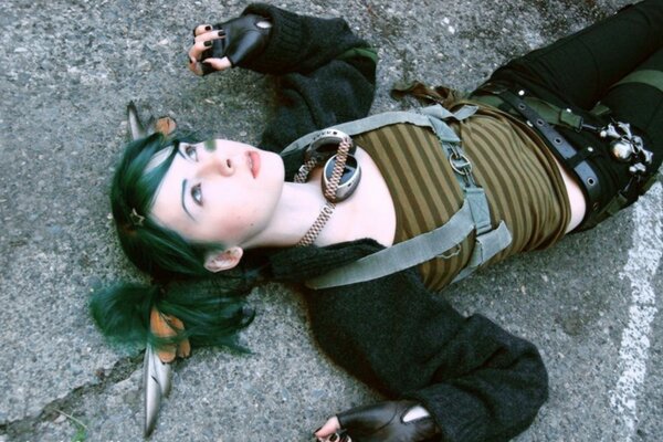 A girl with green hair is lying on the asphalt