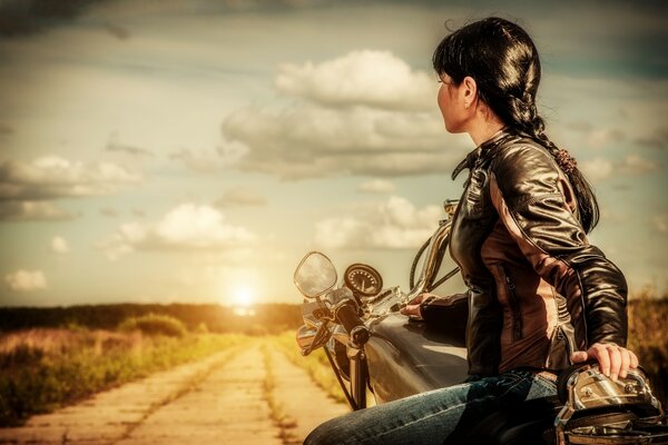 Mädchen auf einem Motorrad fährt in Richtung Sonnenuntergang