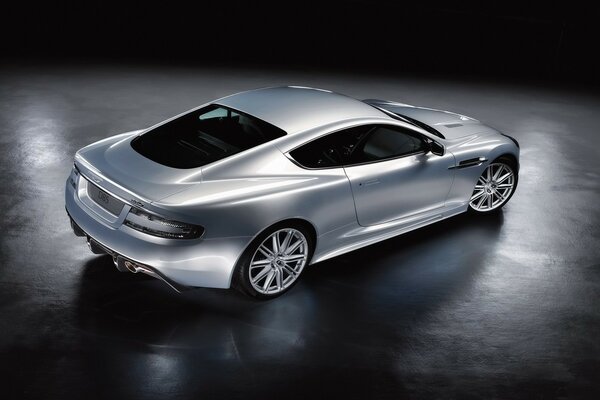 Серебристый Aston Martin DBS стоит по середине комнаты