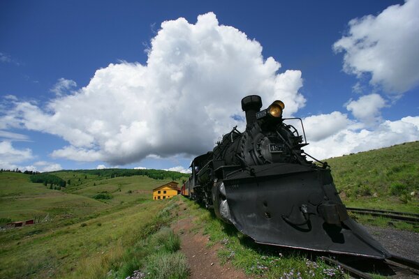 A black locomotive against a blue sky with clouds