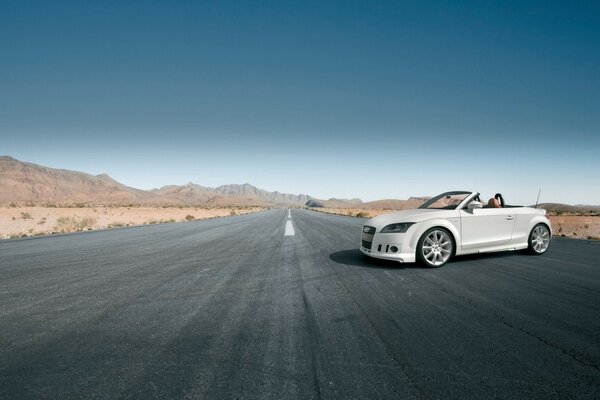 Un elegante Audi convertible blanco en una carretera gris desértica, en el fondo de las montañas