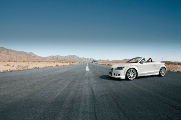 Audi cabriolet blanc chic sur une route grise déserte, sur fond de montagnes