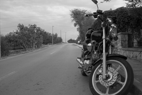 Мотоцикл на фоне безлюдной прогулочной дороги цвета черно-белые