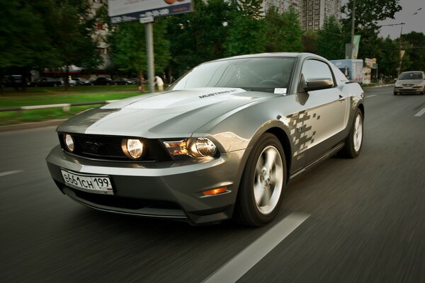 En la pista, un Mustang plateado con faros encendidos