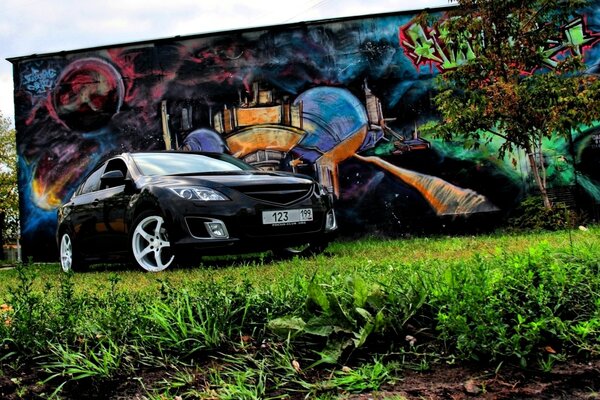 Schwarzer Mazda auf dem Hintergrund von Graffiti und einem kleinen Baum