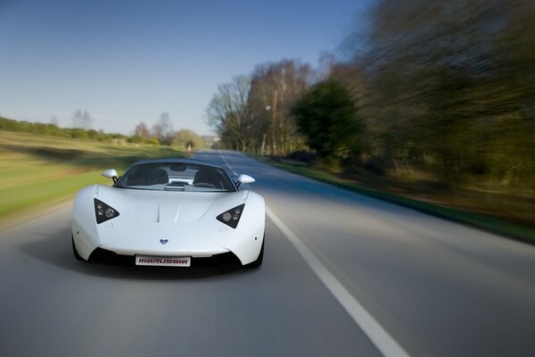 A white car rushes across the asphalt