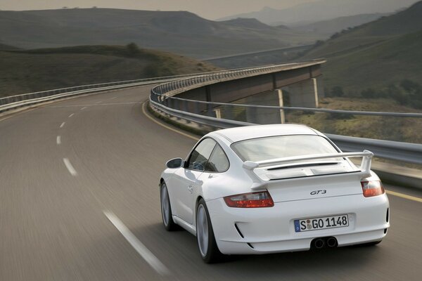 Porsche white 911 GT 3 on the highway in motion against the backdrop of mountain landscapes