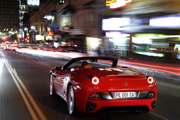 A red Ferrari rushes along the road at high speed at night