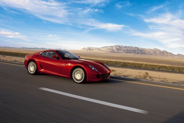 A red Ferrari rushes along the road against the background of a mountain and a blue sky