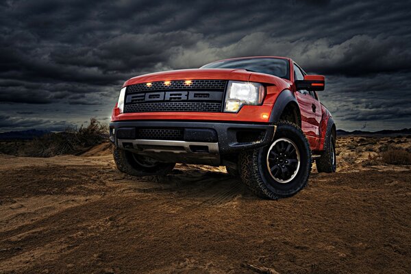 Rotes Ford-Auto auf dem Hintergrund von Sand und Wolken