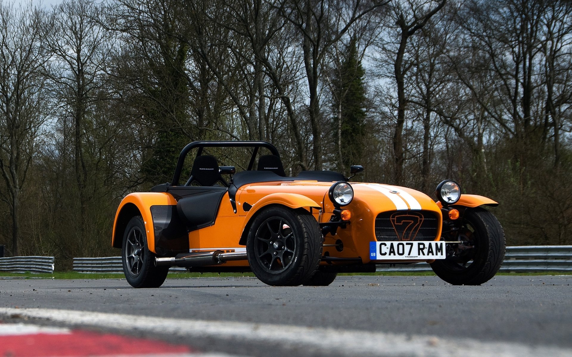 caterham siete supersport caterham seven superdeportivo naranja frente pista de carreras árboles fondo