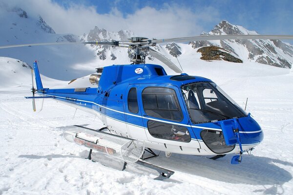 Blauer Hubschrauber in den schneebedeckten Bergen