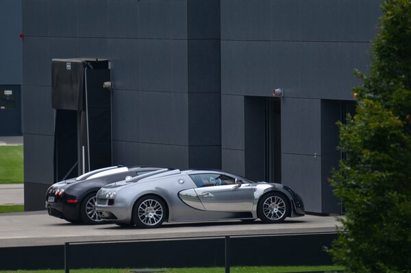 There are three sports cars near the gray building