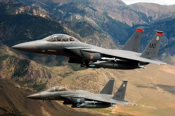 Two Fighter jets are flying over a mountain range