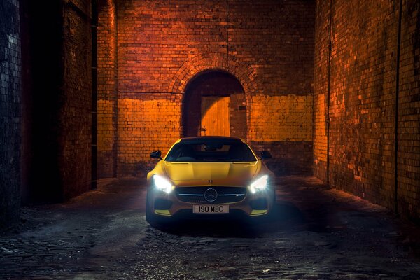 A yellow car stands against a brick wall