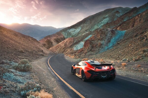 A red car is driving along the road among the mountains