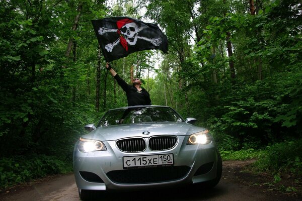 Uomo con bandiera pirata sulla BMW grigia sulla strada forestale