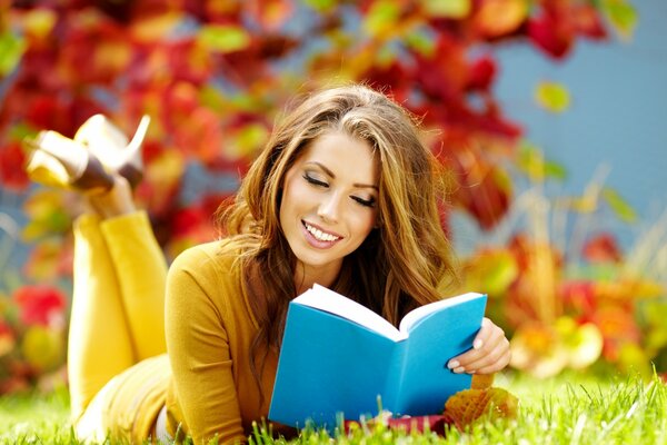 A girl is reading a book lying on the grass