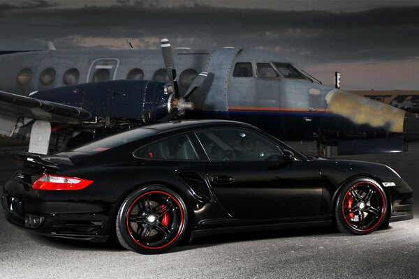 Black Porsche on the background of an airplane in the evening