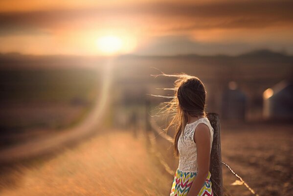 The girl stands by the road and looks into the distance