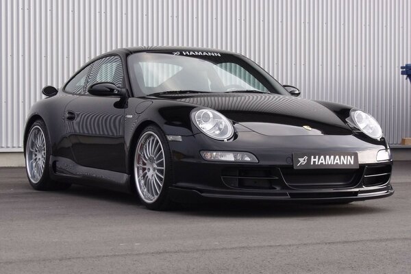 Hamann s black car is parked on the road near the fence