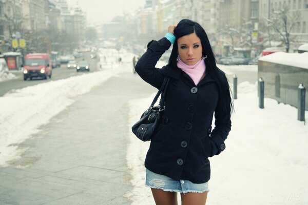 A girl in a short skirt stands against the background of a winter landscape