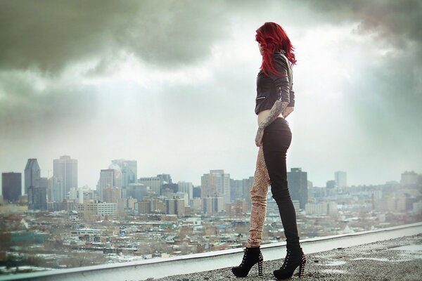 Девушка-модель с рыжими волосами смотрит на серый город