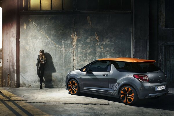 A girl and a citroen car are standing against the wall