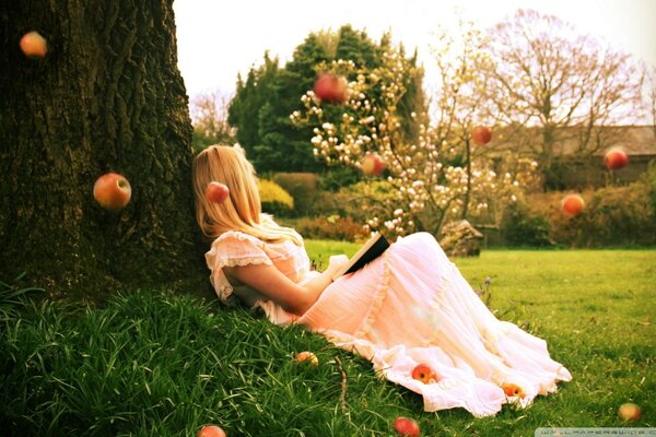 The girl is lying under a tree on the green grass