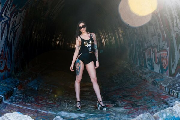 Ein Mädchen mit einem Tattoo am Bein steht im Tunnel