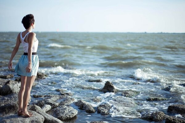 Das Mädchen steht mit dem Rücken auf den Steinen am Meer